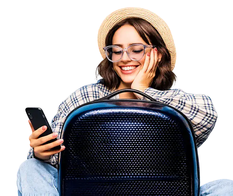 Smiling traveler in a straw hat with a phone and a blue suitcase