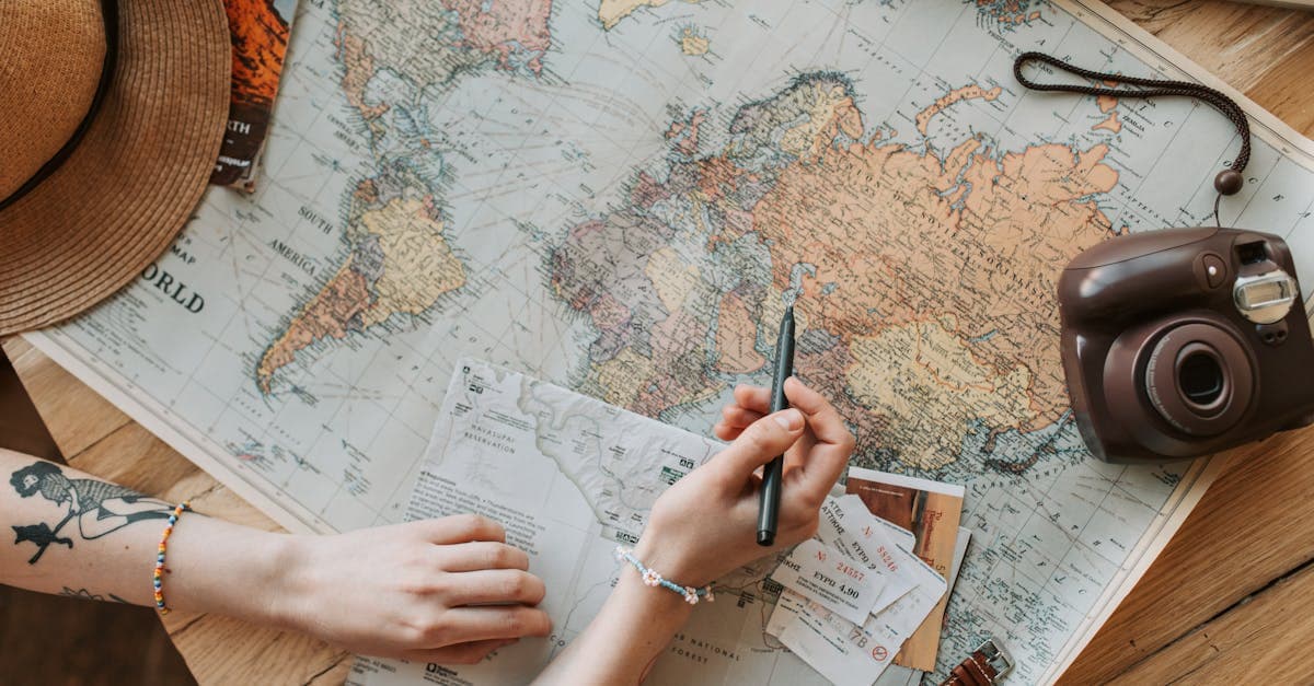 Top view of hands showing how to plan a trip using a map, camera, and travel essentials.