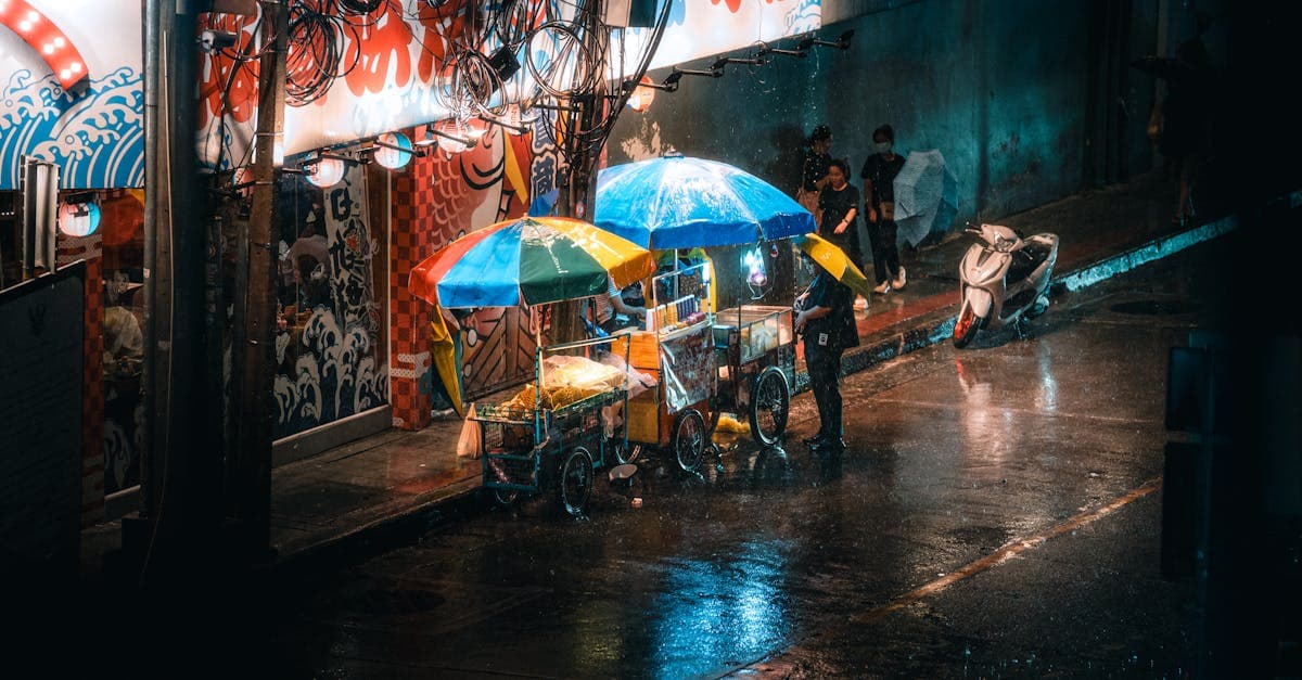 รถเข็นอาหารสตรีทฟู้ดหลากสีตลาดกลางคืนกรุงเทพฯ thailand rainy season แสงไฟสว่างกลางฝนตก