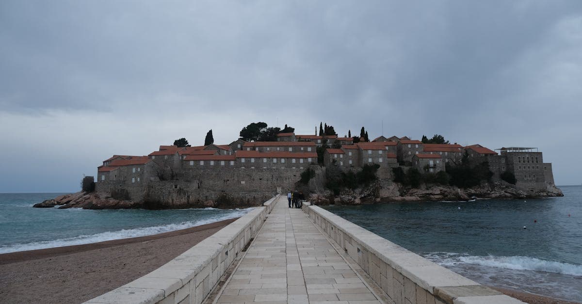 A dramatic view of Sveti Stefan's historic islet and hotels in Montenegro under cloudy skies.