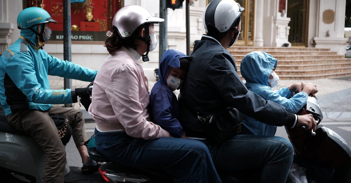 Family in helmets and masks riding a motorbike through Thai city streets, showing essential road safety precautions