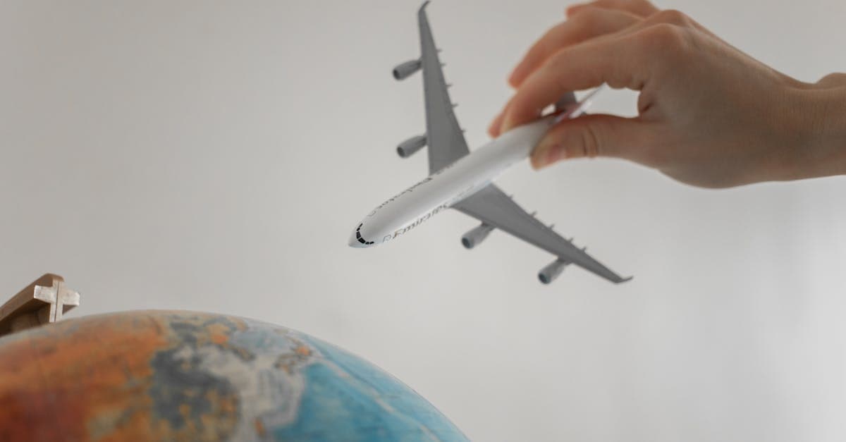 Küre üzerinde oyuncak uçak tutan el, online seyahat sigortası satın alma sürecini simgeliyor.