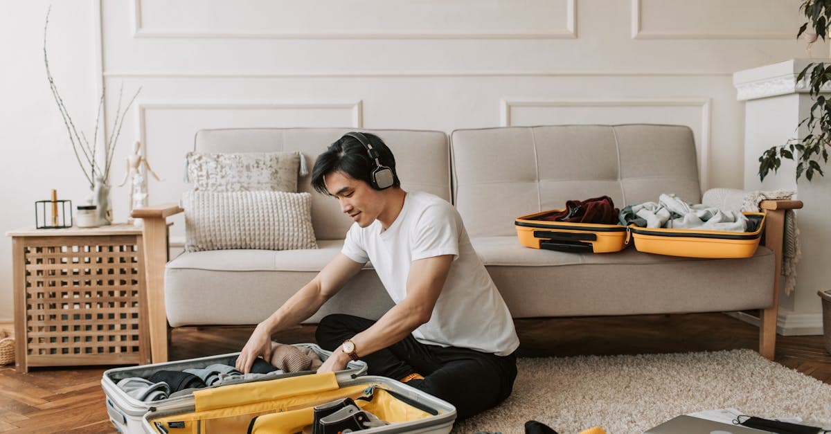 Pria muda mengemas koper di ruang tamu sambil mendengarkan musik, persiapan solo trip.