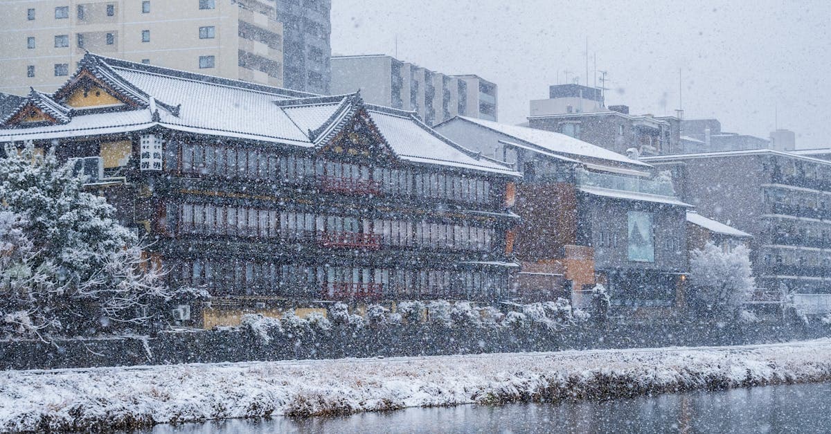 Traditional Japanese wooden building dusted with winter snow beside a calm urban waterway