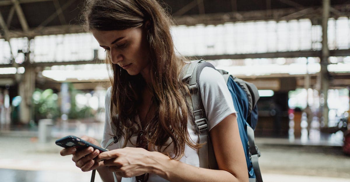 Young woman checking her smartphone at a train station, staying connected while traveling solo.