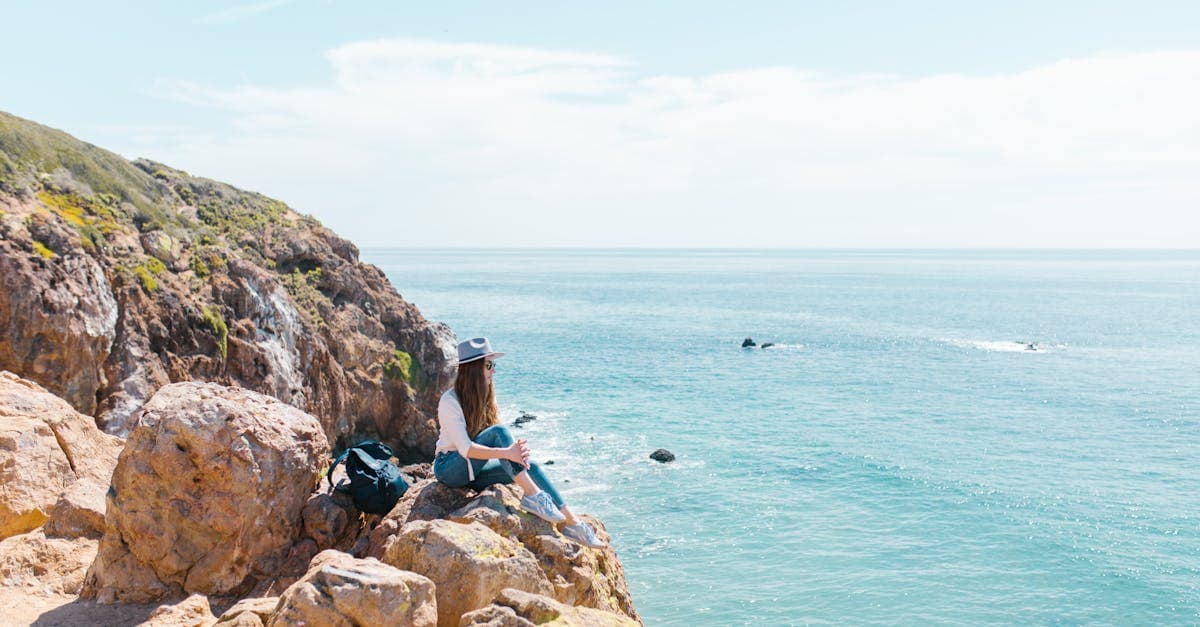 Woman by rocky ocean cliff enjoying nature's tranquility, discovering traveling alone tips for personal wellbeing