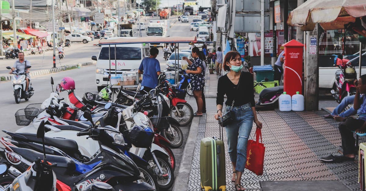 Woman wheeling luggage past parked motorbikes on a bustling Thailand street, prepared for independent travel