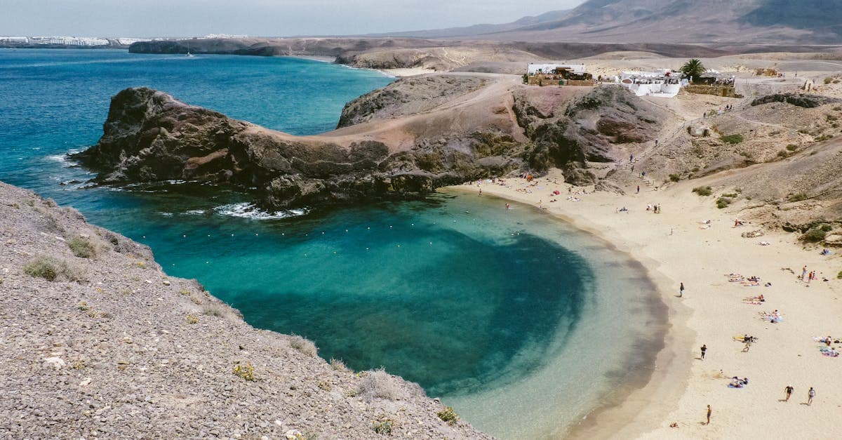Sandy shore beside turquoise ocean and dramatic rocky cliffs, among the top things to do in Lanzarote