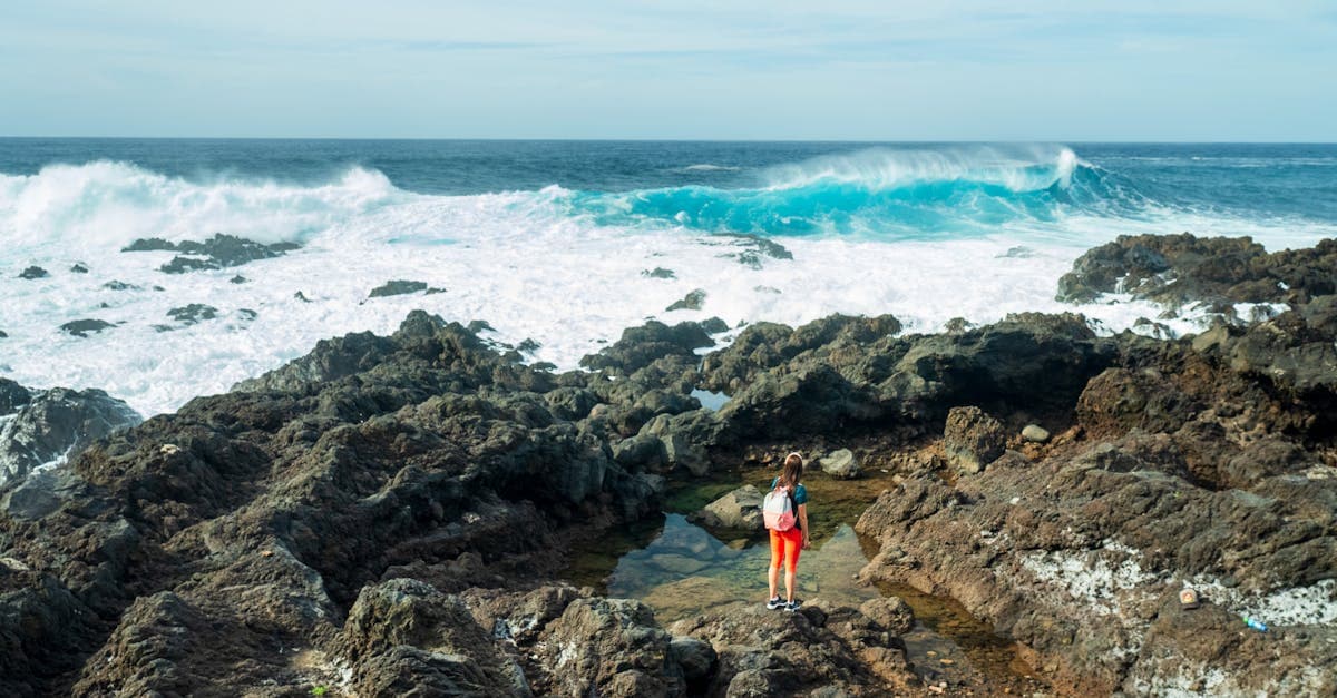 Mujer sola contemplando el mar desde un acantilado rocoso en El Sauzal, España, reflexionando en soledad.