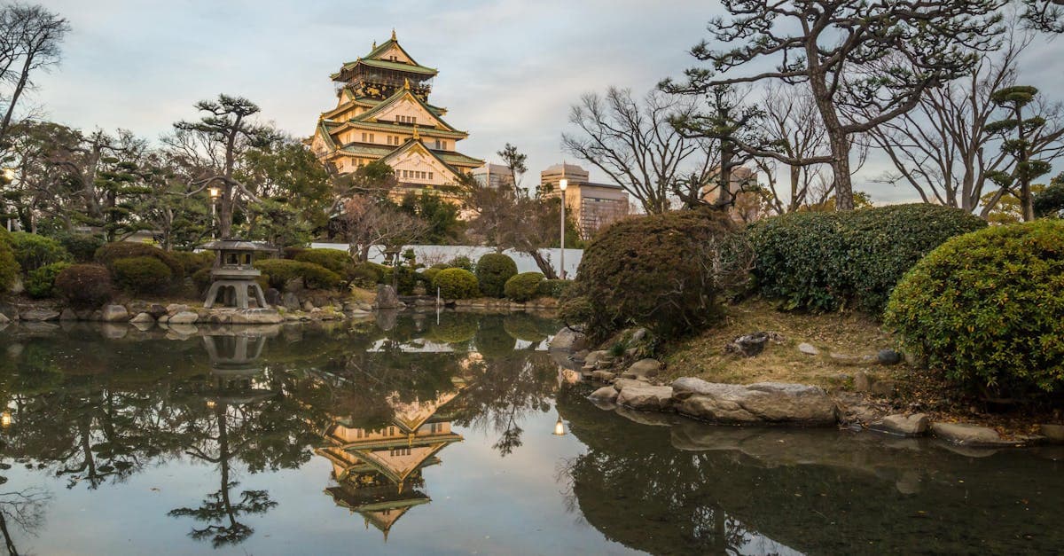Osaka Castle reflecting in a tranquil garden pond at sunset, framing cheap flight season from Singapore to Japan.