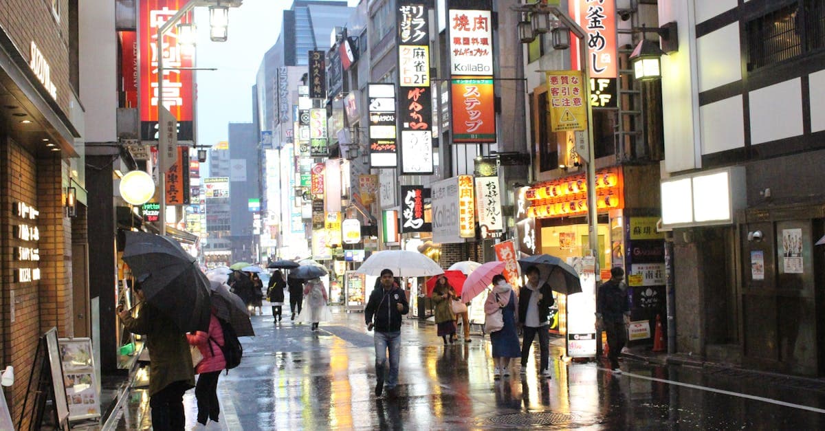 Pejalan kaki berpayung menelusuri jalan Tokyo yang ramai dan bercahaya di malam hari saat hujan