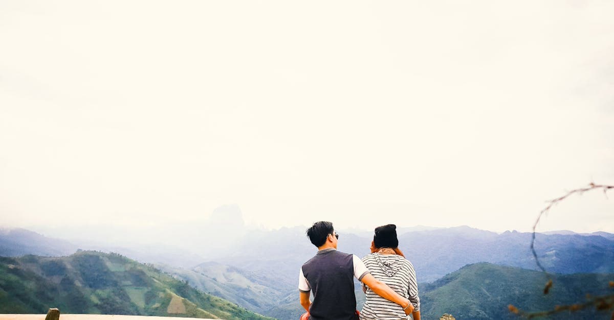 霧がかかる山岳地帯を見渡すベンチで、ヨーロッパ旅行の絶景を堪能するカップル