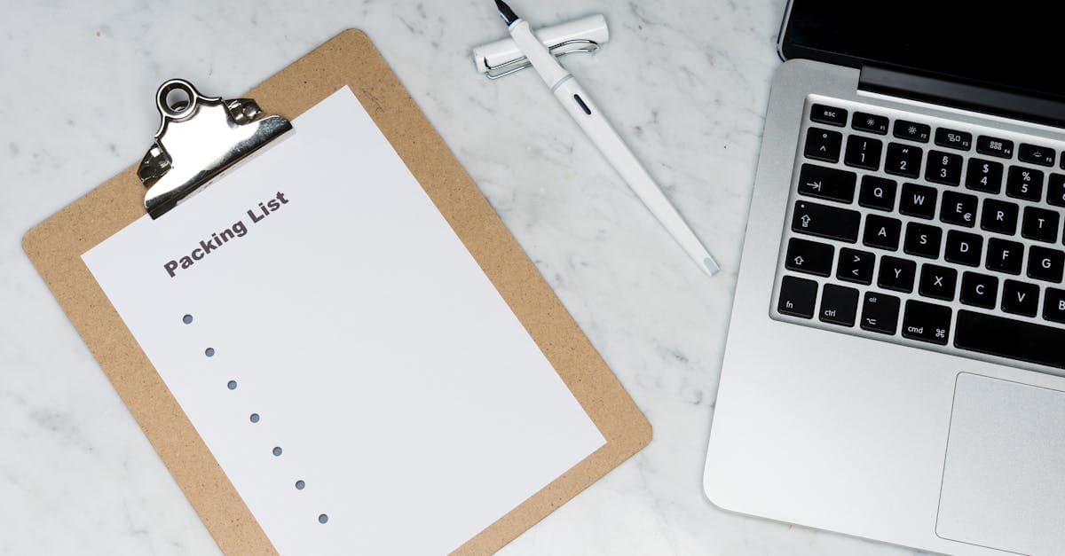 Flat lay packing list clipboard with pen and laptop on a clean marble desk