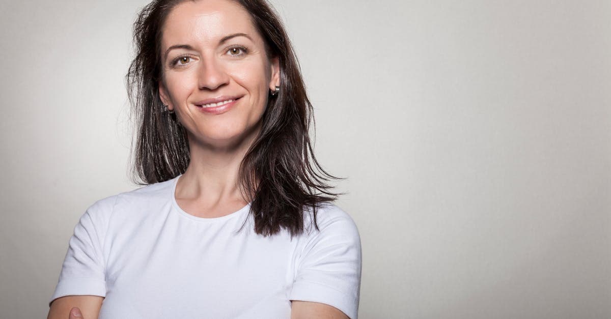 Portrait of a confident woman smiling with arms crossed, wearing a white t-shirt on a gray background.