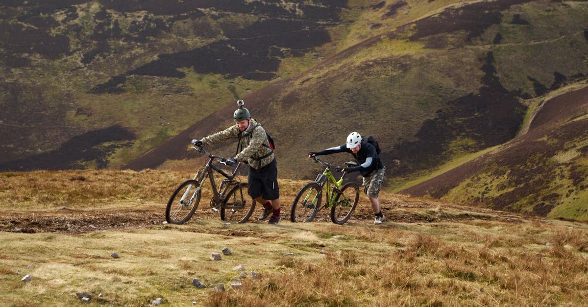 Two cyclists pushing mountain bikes uphill in Scotland's Pentland Hills, an activity often excluded from standard backpacker insurance