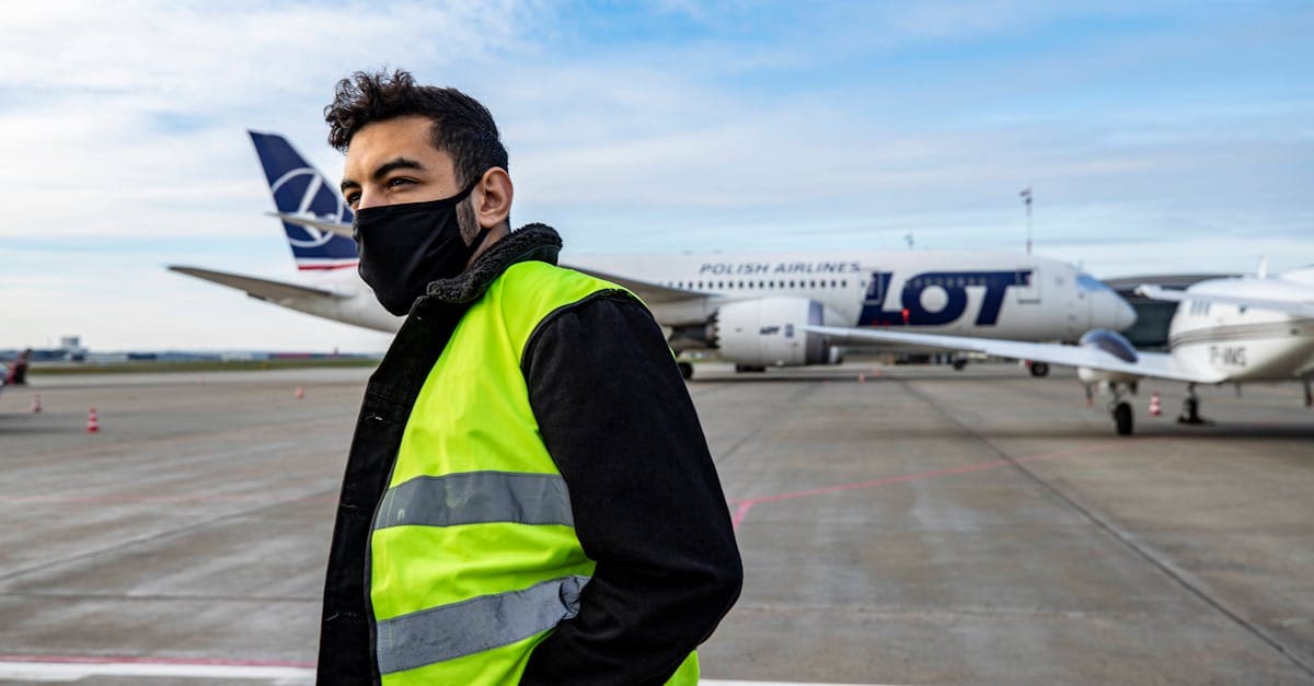 Pracownik lotniska w kamizelce odblaskowej przy samolocie LOT: emigracja zarobkowa Polaków.