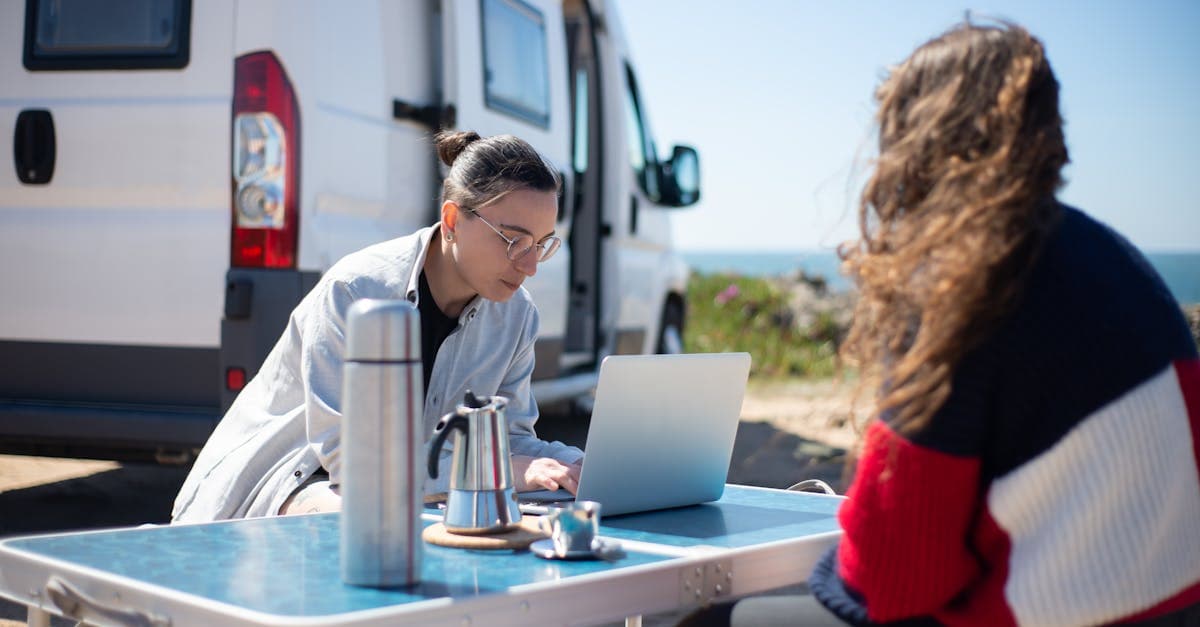 Couple working on a laptop beside a camper van on a Portuguese beach using a portable wifi hotspot