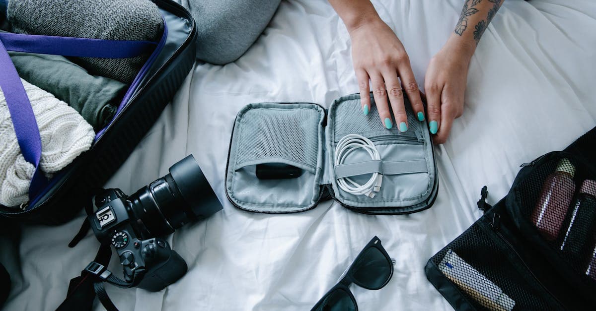 Woman packing electronics, camera and sunglasses in suitcase, travel checklist carry-on essentials.
