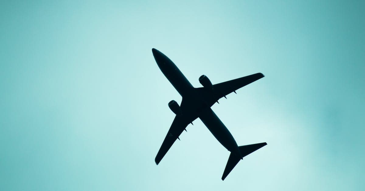 A striking silhouette of an airplane flying overhead against a light blue sky in Mexico City.