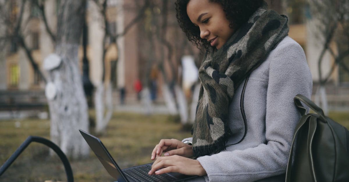 Dışarıda oturan, atkıya sarılı, taşınabilir mobil wifi paketleri araştıran ve dizüstü bilgisayar kullanan genç bir kadın.